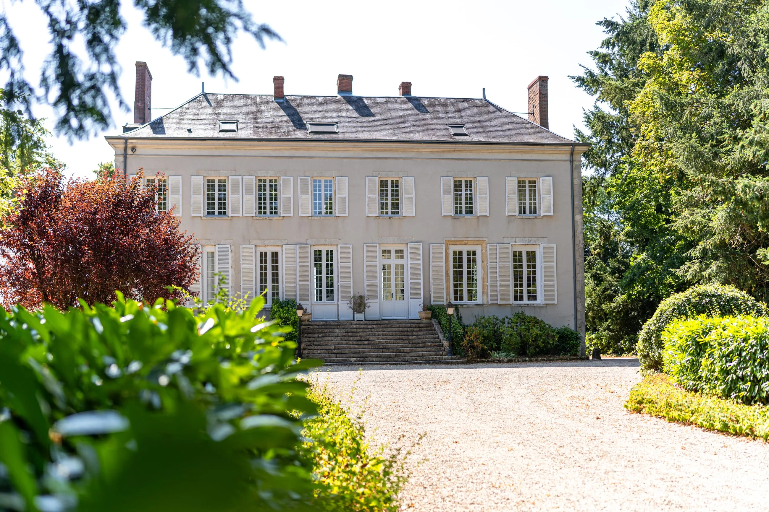 The château facade, pale shutters and a stone perron, at the end of a gravel drive