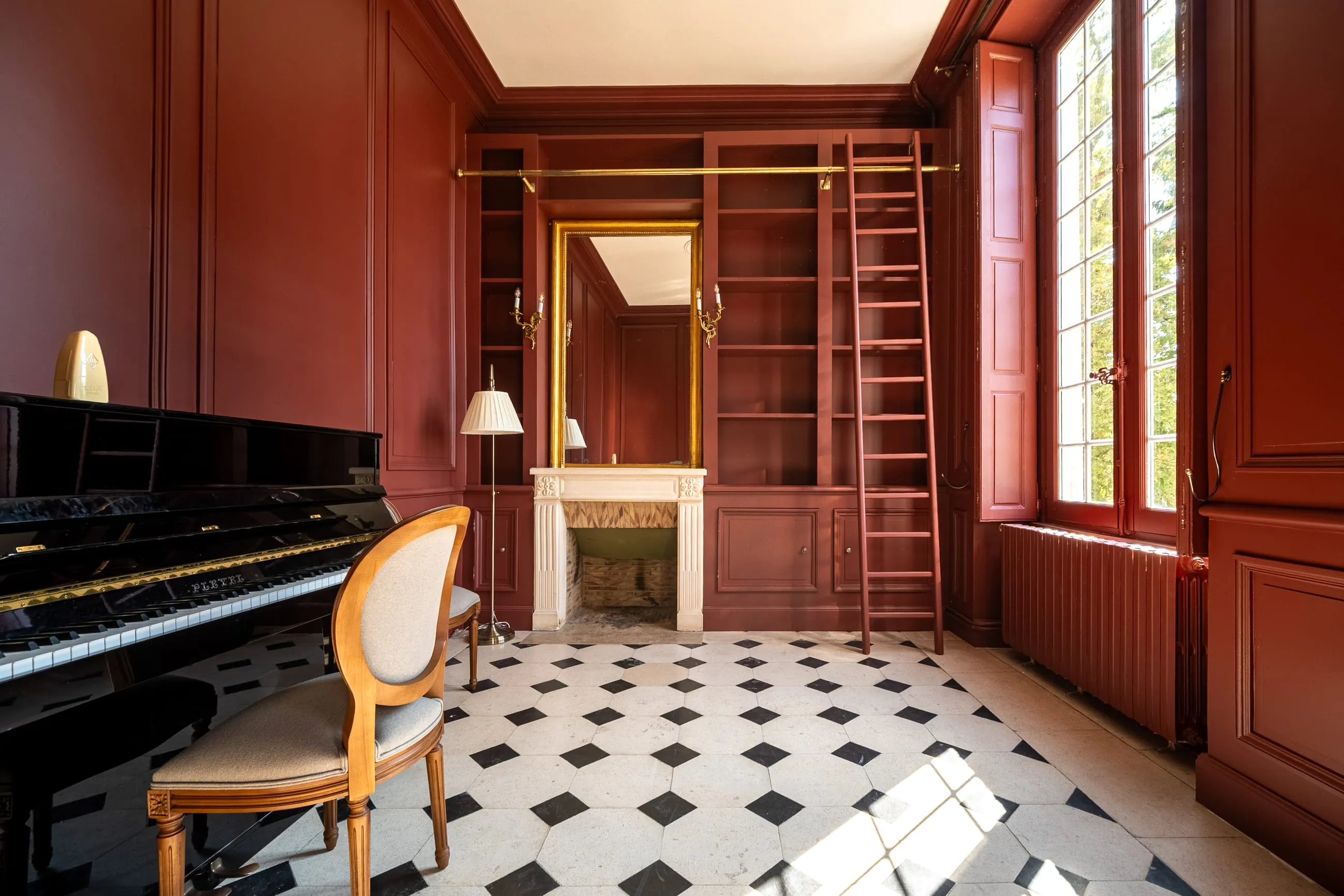 Le grand salon aux boiseries rouges, sa bibliothèque, son échelle et son piano à queue
